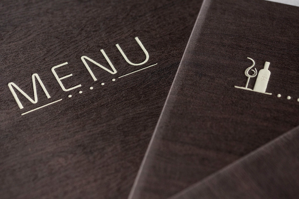 Menu en bois sombre avec mot "MENU" gravé et pictogramme de bouteille et verre sur voie gravée.