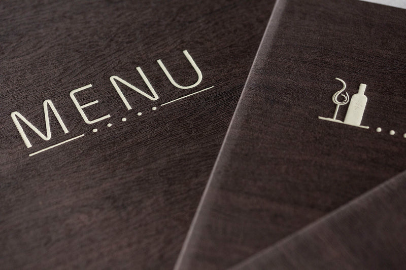 Menu en bois sombre avec mot "MENU" gravé et pictogramme de bouteille et verre sur voie gravée.